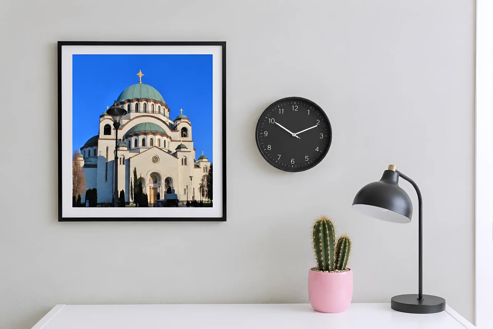Fotografija Hrama Svetog Save u crnom ramu, uz zidni sat, lampu i kaktus